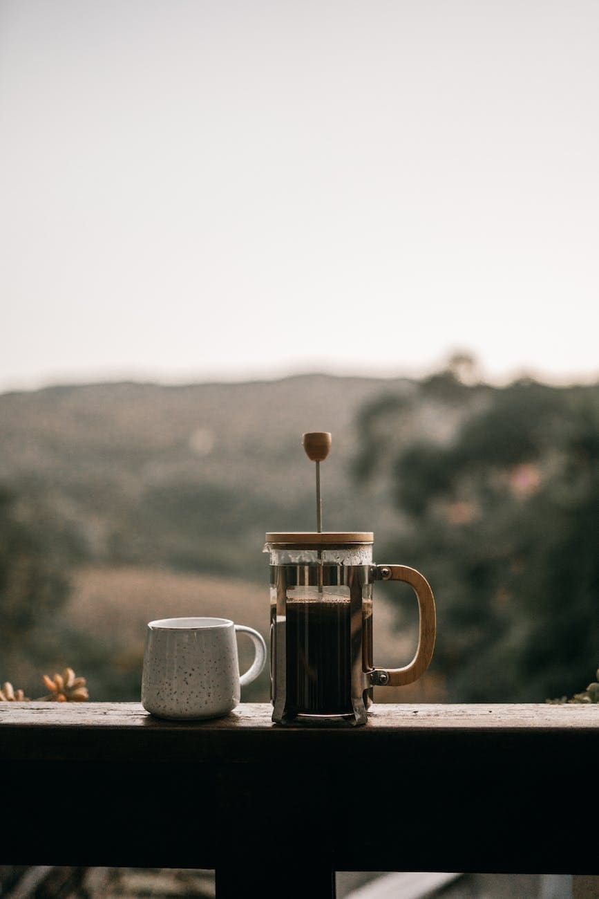 a french press with coffee on a wooden railing